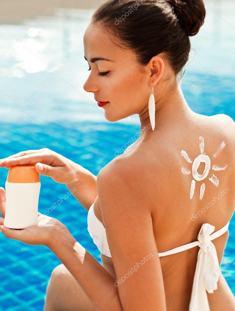 Girl putting sun block near pool holding white sun tan lotion bottle