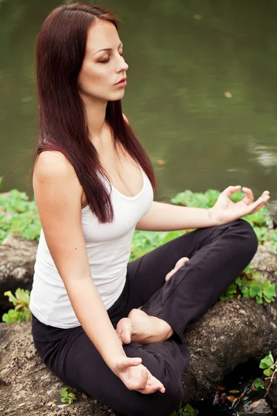 Mujer en forma espiritual sentada en pose de loto sobre una piedra de río — Foto de Stock