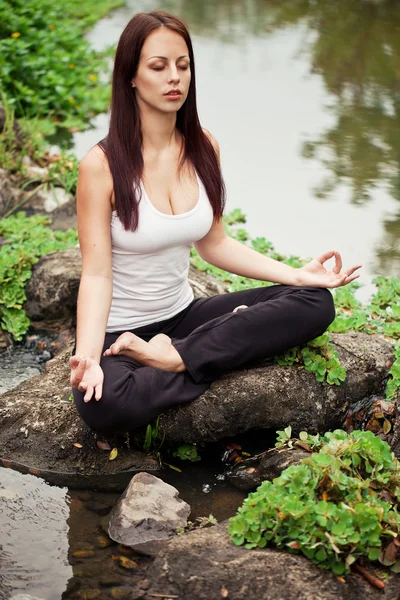 Mujer en forma espiritual sentada en pose de loto sobre una piedra de río — Foto de Stock