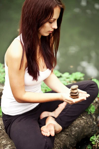 Mujer en forma espiritual sentada en pose de loto sobre una piedra de río — Foto de Stock