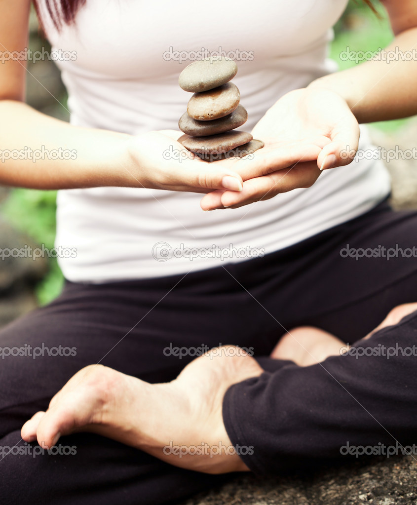 Spiritual fit woman sitting in lotus pose on a river stone