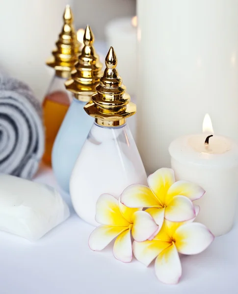 Tres flores de Plumeria con aceite de masaje y bálsamo en tazón, toalla y vela —  Fotos de Stock