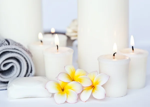 Tre fiori di Plumeria con olio da massaggio e balsamo in ciotola, asciugamano e candela — Foto Stock