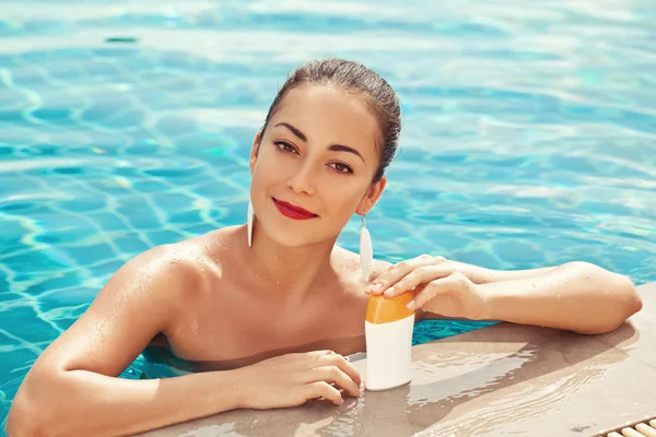 Girl putting sun block near pool holding white sun tan lotion — Stock Photo, Image