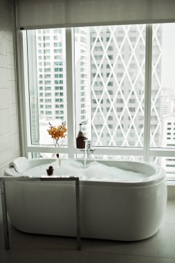 Modern Bathroom interior with white bathtub against huge window with city view clipart