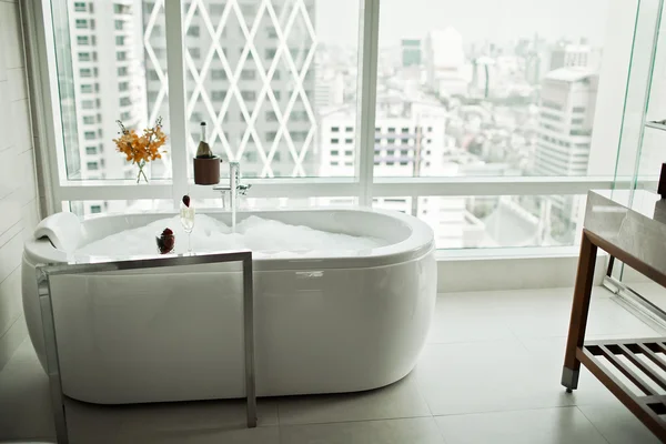 Interior del cuarto de baño moderno con bañera blanca contra ventana enorme con vista a la ciudad —  Fotos de Stock