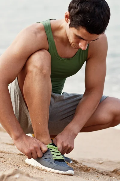 Jeune homme lacer ses baskets sur la plage . — Photo