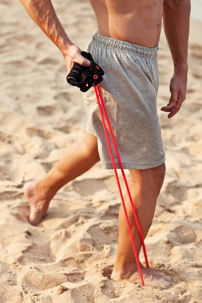 Young athletic man exercising and doing fitness with a chest expander(resistance band ) on the beach — Stock Photo, Image