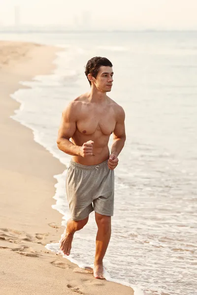 Hombre atlético joven haciendo ejercicio y corriendo en la playa — Foto de Stock