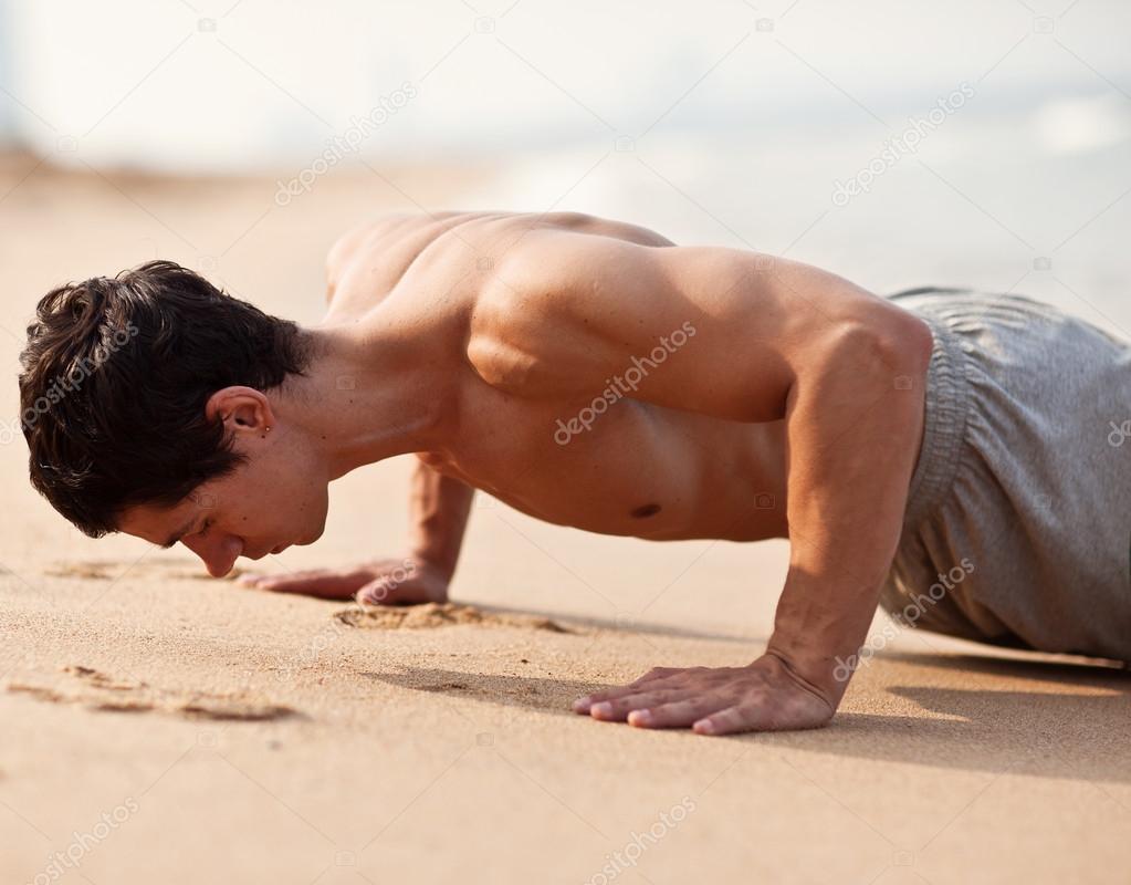 Fitness man exercising push ups. Male fitness model cross-training on beach. Caucasian man in his twenties.