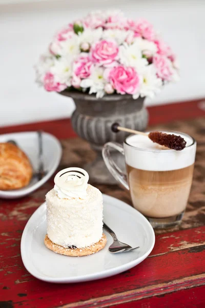 Coconut pastry with flowers, latte and chocolate croissant — Stock Photo, Image