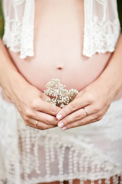 Pregnant woman holding her belly and flower outdoor — Stock Photo, Image