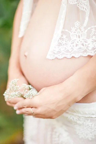 Pregnant woman holding her belly and flower outdoor — Stock Photo, Image