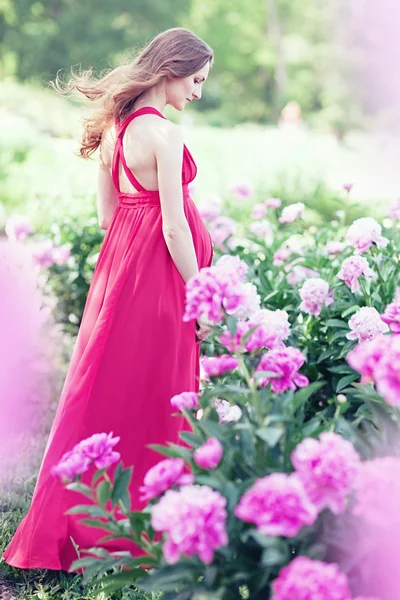 Gravid kvinna i blommande trädgård av pion — Stockfoto