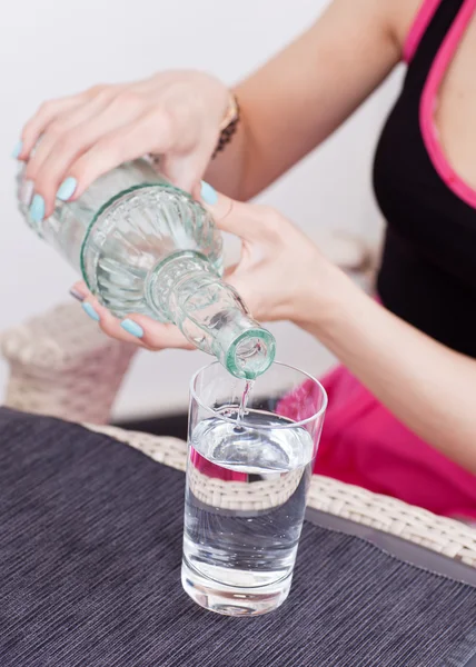 Woda wylewa się z butelki do szkła przez kobieta w różowej sukience — Zdjęcie stockowe