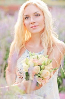 Lavanta sahada oturan sarışın bir bayan. düğün. gelin buketi ile.