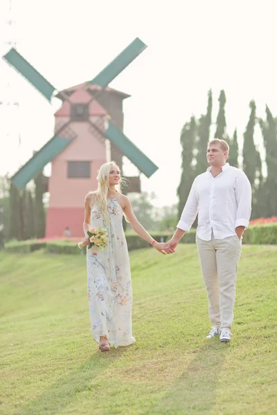 Romantyczna Para spacerująca w dziedzinie trzymając ręce w pobliżu wiatrak — Zdjęcie stockowe