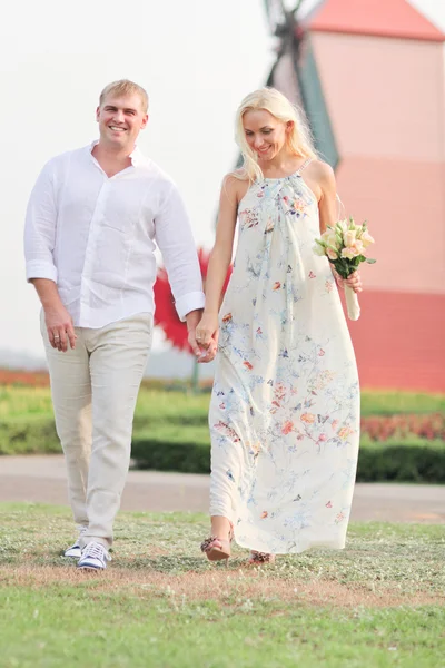 Casal romântico andando em campo segurando as mãos perto do moinho de vento — Fotografia de Stock