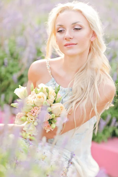 Красивая блондинка сидит на лавандовом поле. Свадьба. Невеста с букетом . — стоковое фото