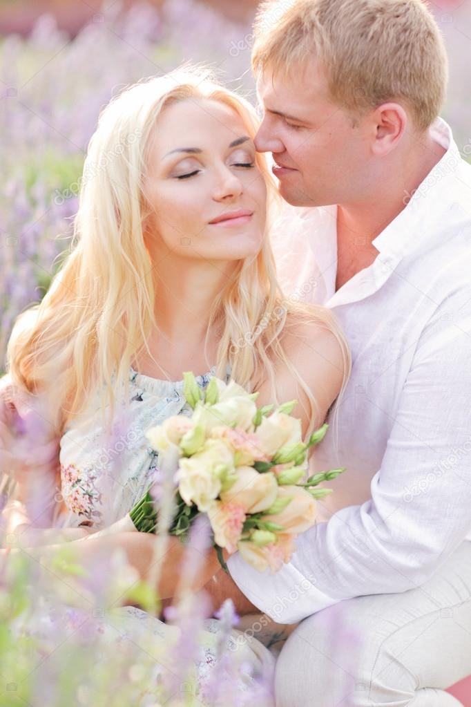 Beautiful happy couple sitting on purple lavender field, having fun on floral glade, summer nature, love concept