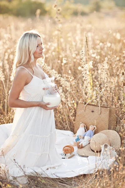Blonďatá žena v bílých šatech s mlékem na přírodu — Stock fotografie
