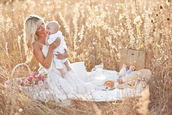 Familia feliz al atardecer. Madre en vestido blanco con bebé en la naturaleza —  Fotos de Stock
