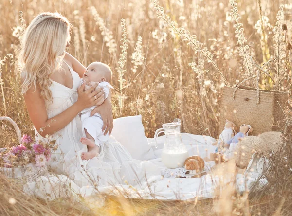 Familia feliz al atardecer. Madre en vestido blanco con bebé en la naturaleza —  Fotos de Stock