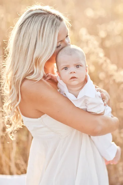 Gelukkige familie op zonsondergang. moeder in witte jurk met baby in de natuur — Stockfoto