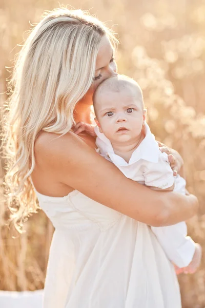 Familia feliz al atardecer. Madre en vestido blanco con bebé en la naturaleza —  Fotos de Stock