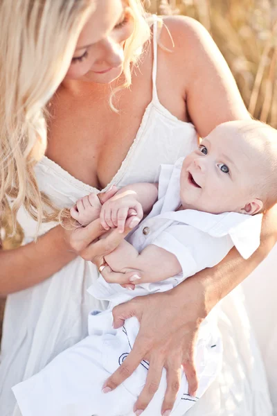 Bonne famille au coucher du soleil. Mère en robe blanche avec bébé dans la nature — Photo