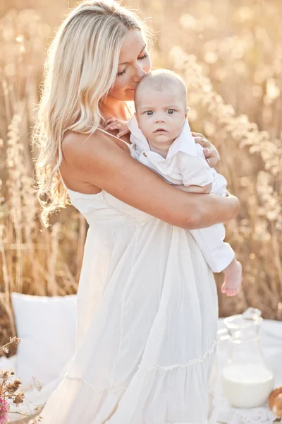 Glückliche Familie bei Sonnenuntergang. Mutter im weißen Kleid mit Baby in der Natur — Stockfoto