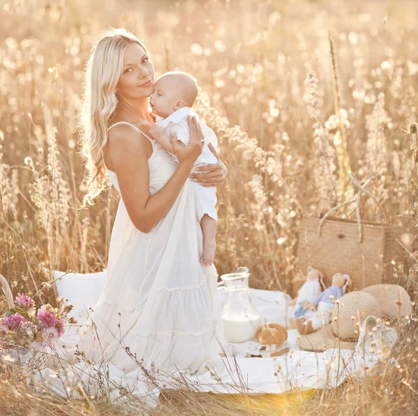 幸福的家庭，在日落。穿白色连衣裙与大自然中的婴儿的母亲 — 图库照片
