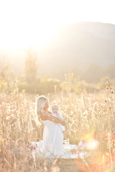 Familia feliz al atardecer. Madre en vestido blanco con bebé en la naturaleza —  Fotos de Stock