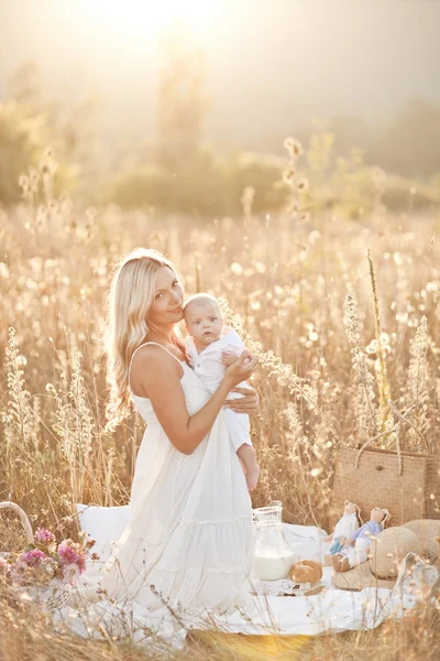 Bonne famille au coucher du soleil. Mère en robe blanche avec bébé dans la nature — Photo