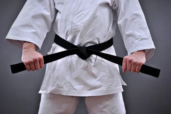 Man in martial arts uniform holding his black belt with both hands — Stock Photo, Image