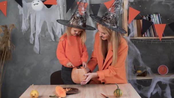 Een vrouw en een meisje in maken een jack-o-lantaarn van grote pompoenen voor de viering van Halloween. Heksenkostuum, hoed. Snijd met een mes, haal de pulp eruit met zaden. Actieve rust thuis. Kinderen — Stockvideo
