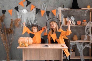 Anne ve kızı cadılar bayramı için kendi elleriyle turuncu ve siyah bayraklardan bir çelenk yaptılar. Odada şenlikli bir dekor.