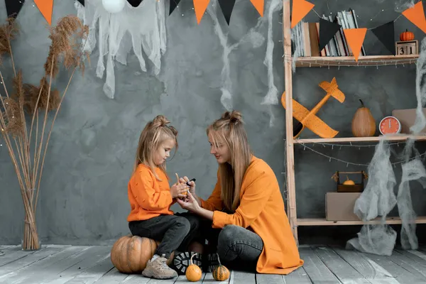 Küçük kız evde annesiyle Cadılar Bayramı süslemesi yapıyor. Mutlu aile anne ve kızı birlikte fener yapıyor. Balkabağına korkunç bir yüz çiziyor ve tatilin tadını çıkarıyor. Cadı kostümü.