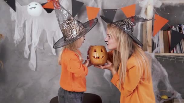 Halloween-Konzept. Kaukasische Familienmutter in Nahaufnahme und Tochter mit Make-up in Kostümen und Hexenhüten feiern Halloween-Posieren mit Kürbisjack. — Stockvideo