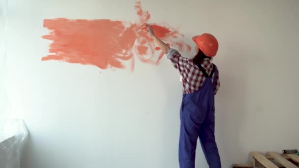 La fille fait des réparations dans l'appartement. Maison déménageant dans un nouvel appartement. Un travailleur fait des réparations, porte un casque orange et peint le mur en orange avec une brosse. — Video