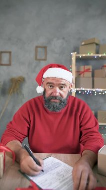 Çevrimiçi ticaret. Noel Baba şapkalı ve beyaz sakallı beyaz bir adam video iletişimiyle internetten mal siparişi alıyor. Dikey video. Noel ya da yeni yıl için tatil indirimi kavramı.