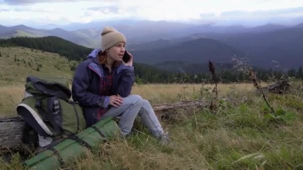 Retrato de una joven turista feliz llamando por teléfono durante un alto en la cima de la montaña. — Vídeos de Stock