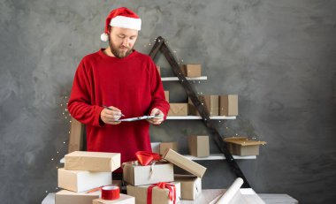 Noel Baba şapkası takan beyaz sakallı adam ve evde çalışan kırmızı kazak sahibi. Noel hediyesi alışverişi konsepti. Dağıtım için kutucukları işaretle.