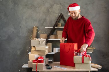 Noel Baba şapkası takan küçük bir işletme sahibi Noel için bir çanta dolusu hediye toplar. Kış tatilinin arifesinde çevrimiçi sipariş teslimatı. Satış ve girişimci. Tatil ve sürpriz konsept