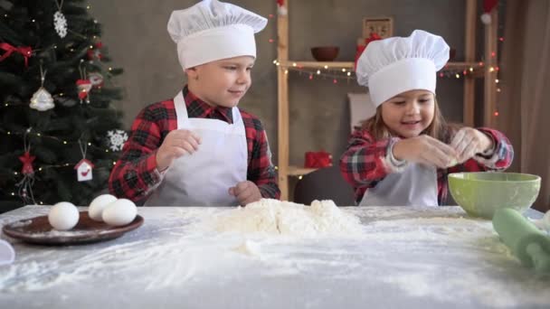 Linda niña rompe el huevo en harina para cocinar y amasar la masa. Niños vestidos como chefs preparan pasteles caseros en la cocina. — Vídeos de Stock