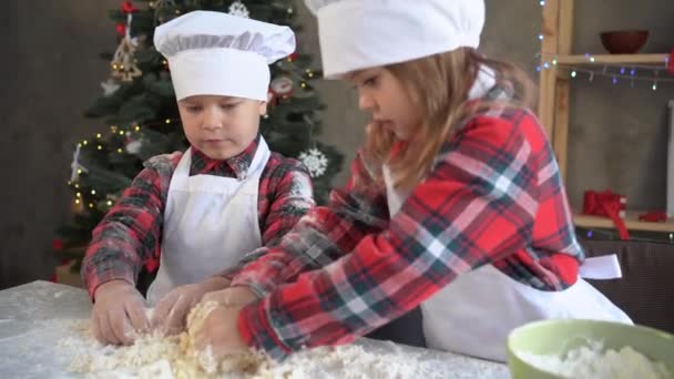 Dwoje dzieci gotuje ciasto ugniatające na stole. chłopiec i dziewczyna przygotować ciasto do pieczenia w domu na Boże Narodzenie ciasteczka. Brat siostra w postaci kucharza — Wideo stockowe