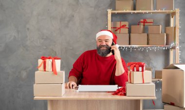Evde çalışan Noel Baba şapkalı bir adam Noel günü teslimat için internetten sipariş alıyor. Mutlu Küçük İşletmeler Yeni Yıl Satışı. Noel için depo konsepti