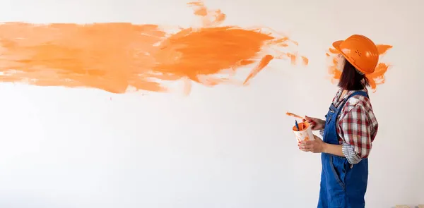 修理一个新的家庭妇女修理工 用刷子在墙上涂上橙色的油漆 白人女孩在房间里做墙面装饰 翻新工程的概念 班纳案文的位置 — 图库照片