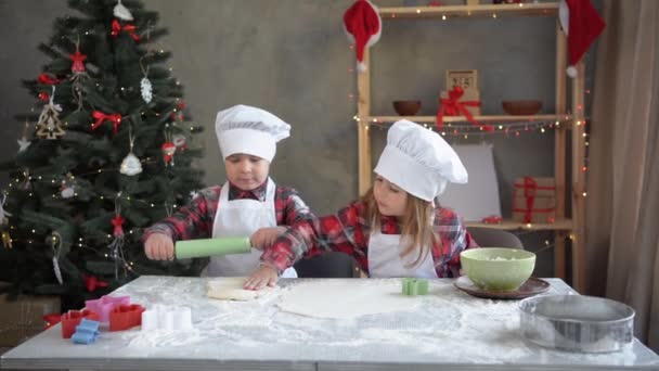 Kinder rollen Teig aus, um selbst gebackene Weihnachtsplätzchen zu backen. Kochen zu Hause mit Kindern. Bruder und Schwester in Form eines Bäckers kochen den Prozess — Stockvideo