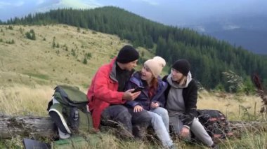 Bir grup yürüyüşçü bir dağın tepesinde durup devrilmiş bir ağaca oturur ve uygulamayı kullanarak bir akıllı telefondan selfie çeker..